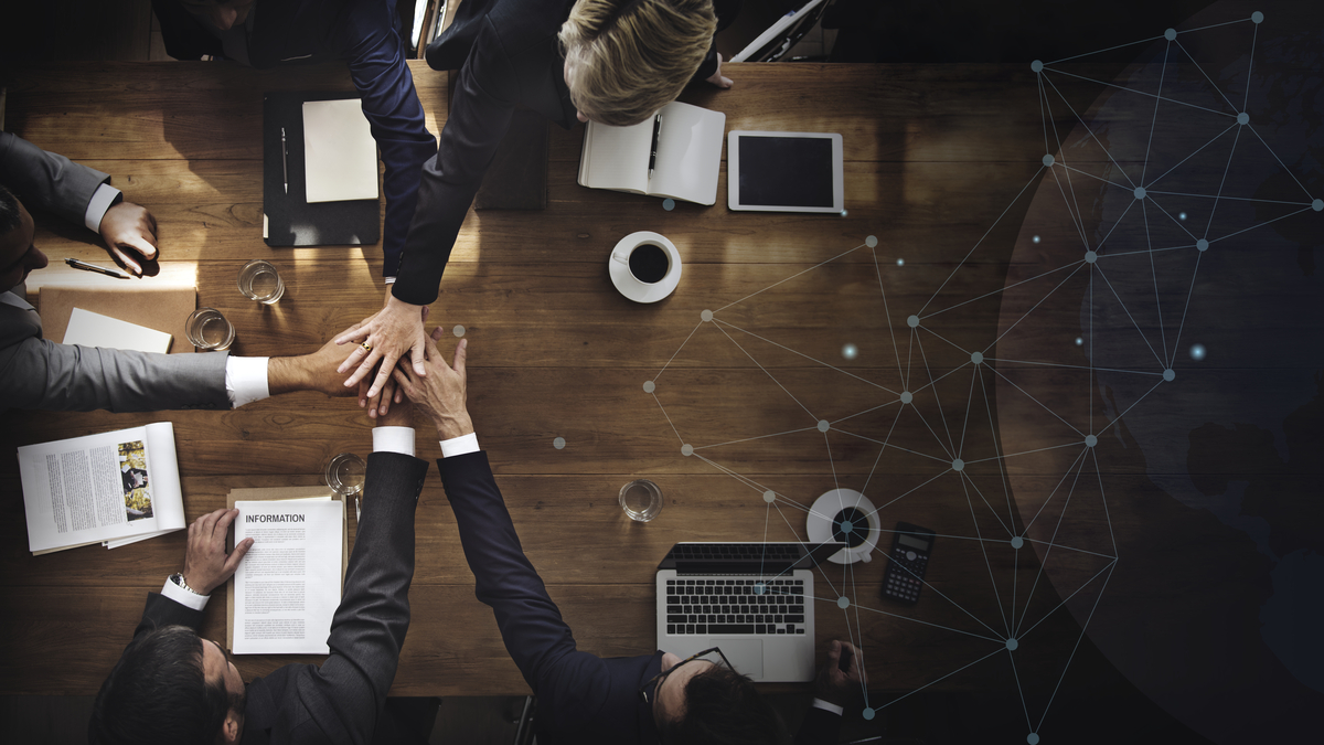 Cinco pessoas de mãos dadas, representando o networking de negócios e a importância deste conceito.