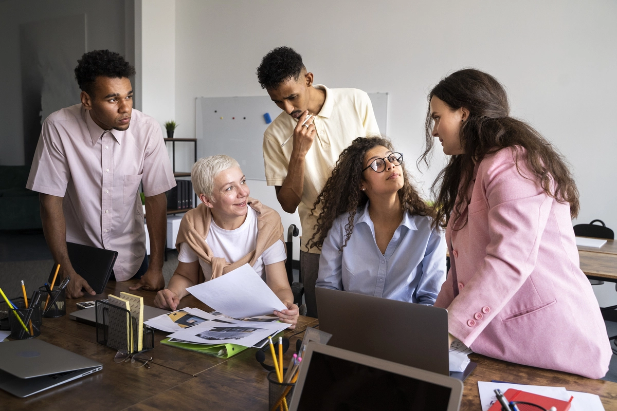 Cinco pessoas de etnias e idades diferentes, representando os benefícios da diversidade e inclusão no ambiente de trabalho.