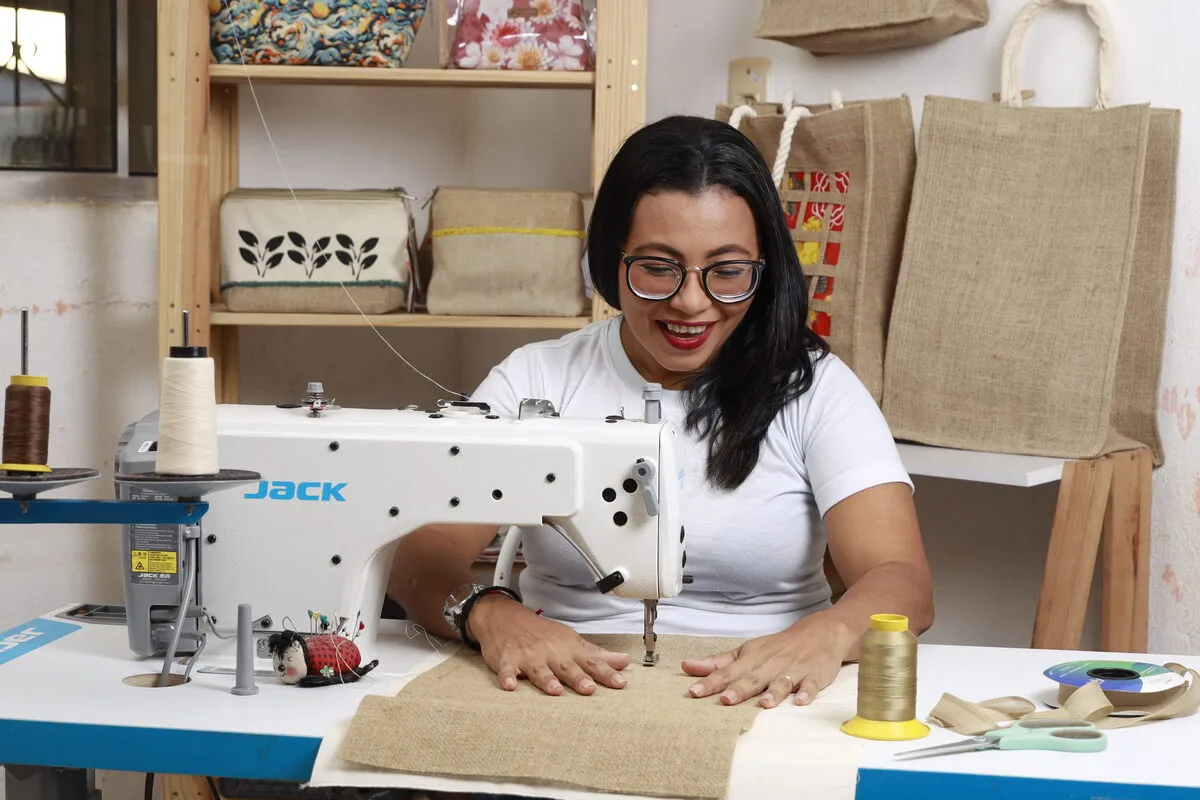 Uma mulher usando uma máquina de costura, sorrindo por ter uma consultoria para registro de marca da empresa dela ao lado.