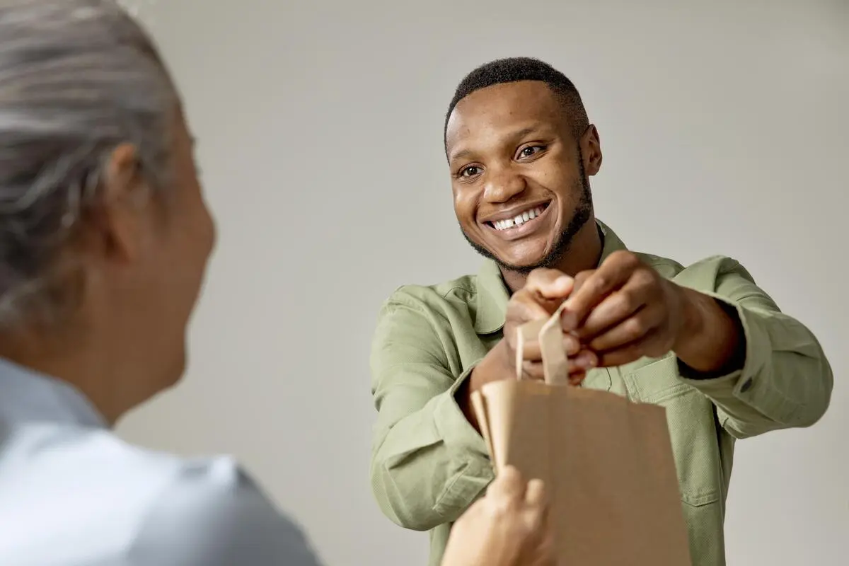 Um homem sorrindo entregando uma sacola para uma senhora, representando a fidelização de clientes em uma loja.