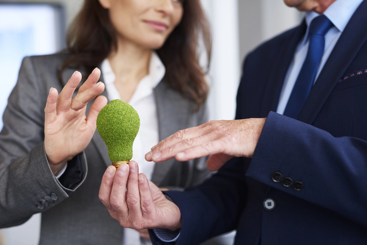 Empresários segurando uma lâmpada ecológica, simbolizando inovação sustentável nos negócios.